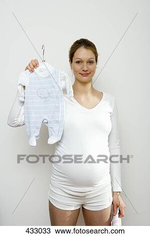 Stock Image - Pregnant woman holding up a blue baby outfit. Fotosearch
