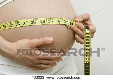 Stock Image - Pregnant woman measuring her stomach with a tape measure. Fotosearch