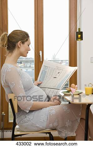 Stock Image - Pregnant woman reading a newspaper over breakfast. Fotosearch
