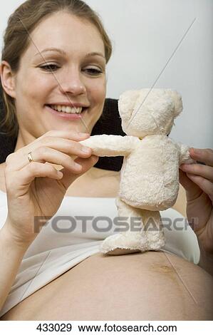 Stock Photo - Pregnant woman sitting down and holding a teddy bear. Fotosearch