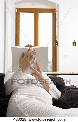 Stock Photo - Pregnant woman sitting on a sofa reading a book. Fotosearch