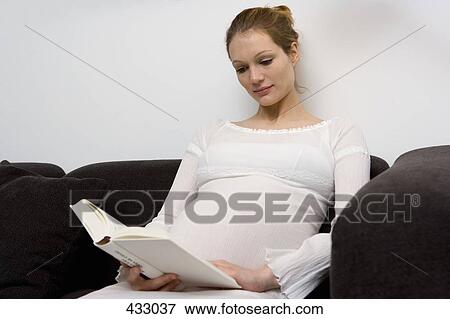 Pregnant woman sitting on a sofa reading a book View Large Photo Image Stock Photo - Pregnant woman sitting on a sofa reading a book. Fotosearch
