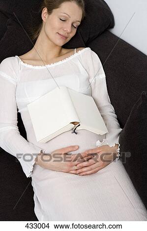 Picture - Pregnant woman sleeping on a sofa with a book on her stomach. Fotosearch