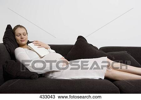Stock Image - Pregnant woman sleeping on a sofa with a book on her chest. Fotosearch