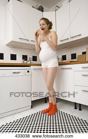 Pregnant woman standing in a kitchen eating a sandwich View Large Photo Image Stock Photo - Pregnant woman standing in a kitchen eating a sandwich. Fotosearch