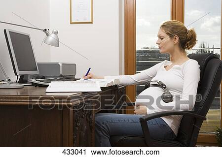 Stock Image - Pregnant woman working from home with headphones on her stomach. Fotosearch