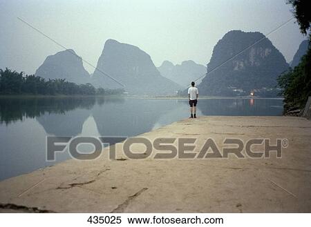Man standing at the edge of a lake in front of rock formations, Yangshou, China View Large Photo Image Stock Photography - Man standing at the edge of a lake in front of rock formations, Yangshou, China. Fotosearch