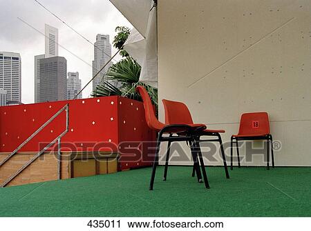 Stock Image - Plastic chairs on terrace with cityscape behind, Singapore. Fotosearch