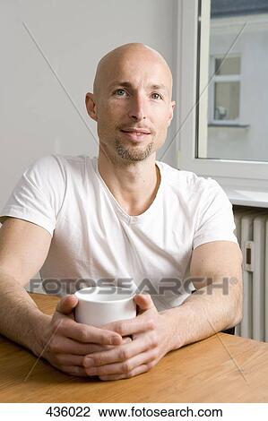 Stock Image - A man sitting at table holding a mug. Fotosearch