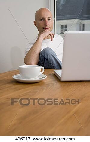 A man sitting at table with laptop and drink View Large Photo Image Stock Photo - A man sitting at table with laptop and drink. Fotosearch