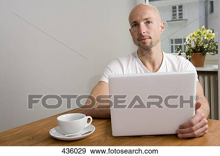 A man sitting at table with laptop and drink View Large Photo Image Stock Photo - A man sitting at table with laptop and drink. Fotosearch