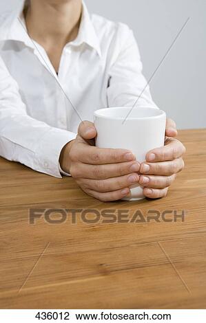 Woman sitting at a table holding a mug View Large Photo Image Stock Image - Woman sitting at a table holding a mug. Fotosearch