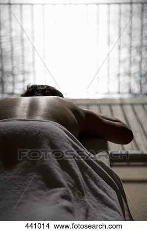 Picture - A man lying down on a massage table. Fotosearch