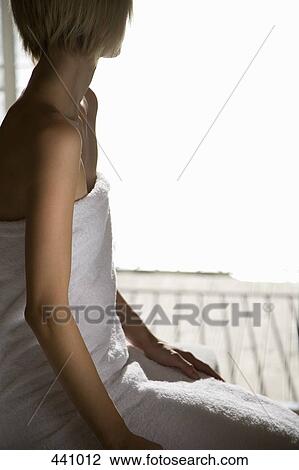 Stock Image - A woman wrapped in a towel and sitting at the edge of a massage table. Fotosearch