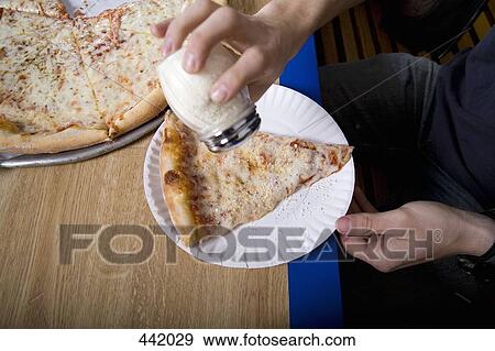 Stock Photo - Person pouring salt onto a slice of pizza. Fotosearch