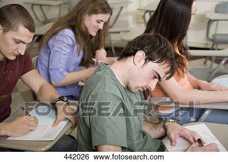 Students sitting at desks and writing View Large Photo Image Stock Photograph - Students sitting at desks and writing. Fotosearch