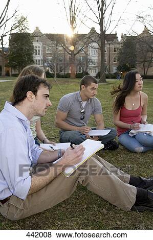 Stock Photo - University students sitting on grass writing. Fotosearch