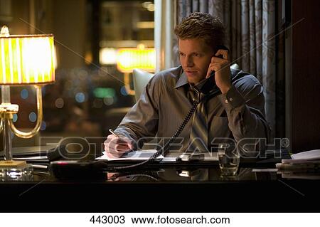 Businessman sitting at a desk and using a telephone View Large Photo Image Stock Image - Businessman sitting at a desk and using a telephone. Fotosearch