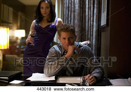 Stock Photo - Businessman sitting at a desk with a woman standing behind him holding a glass of wine. Fotosearch