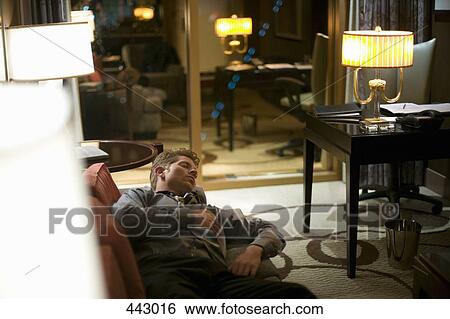 Stock Photograph - Businessman sleeping on a sofa in a hotel room. Fotosearch