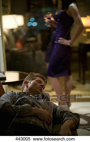 Businessman sleeping on a sofa whilst a woman stands impatiently in the background View Large Photo Image Stock Photography - Businessman sleeping on a sofa whilst a woman stands impatiently in the background. Fotosearch