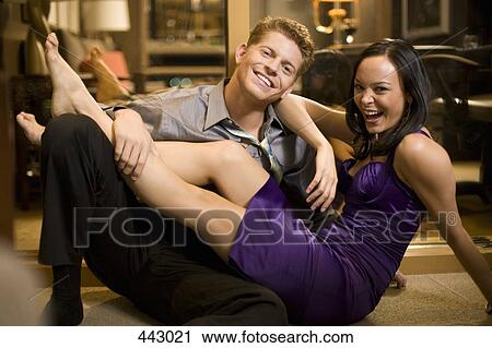 Stock Image - Young woman sitting with her legs across a young man in a hotel room. Fotosearch