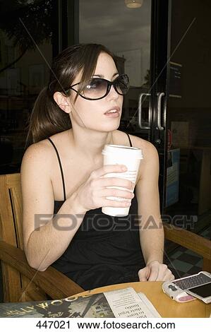 A woman sitting at a cafe holding a cup of coffee View Large Photo Image Stock Image - A woman sitting at a cafe holding a cup of coffee. Fotosearch