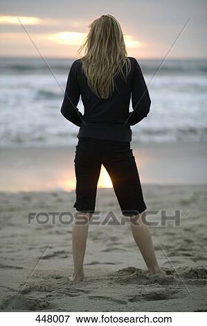 A woman standing on a beach at sunset View Large Photo Image Stock Photo - A woman standing on a beach at sunset. Fotosearch