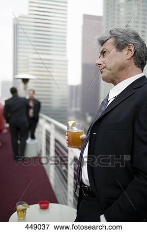 Businessman holding a drink at a roof top bar View Large Photo Image Stock Photo - Businessman holding a drink at a roof top bar. Fotosearch