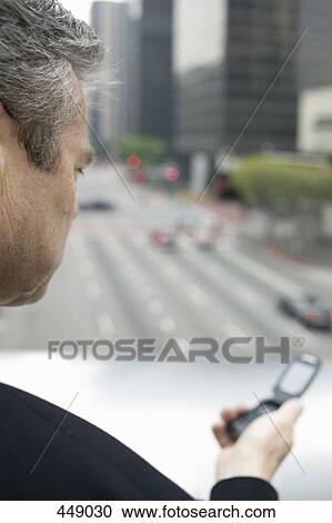Businessman holding a mobile phone on a balcony in the financial district View Large Photo Image Stock Image - Businessman holding a mobile phone on a balcony in the financial district. Fotosearch