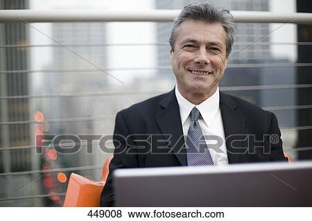 Businessman sitting on a rooftop and working on a laptop View Large Photo Image Stock Photo - Businessman sitting on a rooftop and working on a laptop. Fotosearch