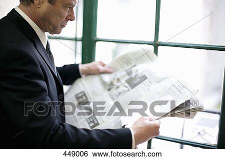 Businessman standing by a window reading a newspaper View Large Photo Image Stock Photograph - Businessman standing by a window reading a newspaper. Fotosearch