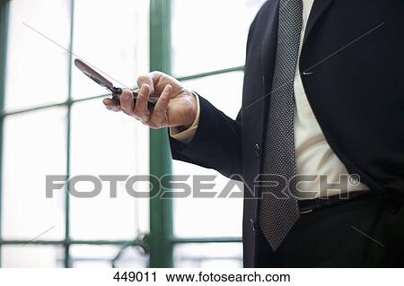Businessman standing by a window using a mobile phone View Large Photo Image Stock Image - Businessman standing by a window using a mobile phone. Fotosearch