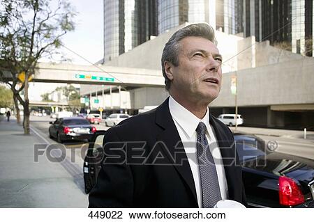 Stock Image - Businessman standing on a city street and looking up. Fotosearch