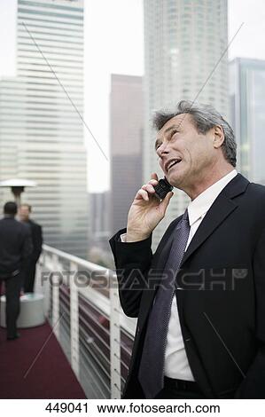 Businessman standing on a rooftop terrace using a mobile phone View Large Photo Image Stock Image - Businessman standing on a rooftop terrace using a mobile phone. Fotosearch