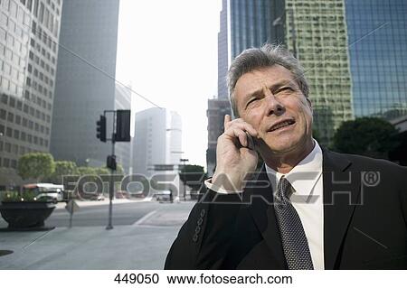 Stock Image - Businessman standing on a street corner using a mobile phone. Fotosearch