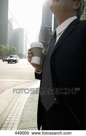 Businessman standing on a street corner holding a cup of coffee View Large Photo Image Stock Photography - Businessman standing on a street corner holding a cup of coffee. Fotosearch