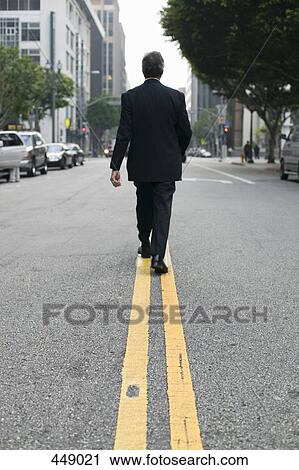 Businessman walking along dividing line on a city street View Large Photo Image Stock Image - Businessman walking along dividing line on a city street. Fotosearch