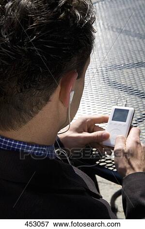 Businessman sitting at an outdoor cafe listening to an MP3 player View Large Photo Image Stock Photo - Businessman sitting at an outdoor cafe listening to an MP3 player. Fotosearch