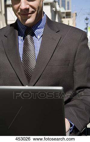 Businessman sitting on an outside bench using a laptop View Large Photo Image Stock Photograph - Businessman sitting on an outside bench using a laptop. Fotosearch