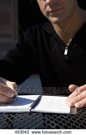 Stock Image - Man sitting outdoors at a table and writing in a personal organizer. Fotosearch