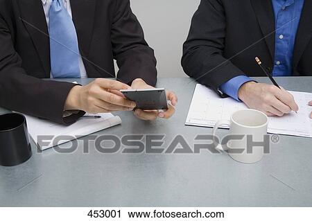 Stock Image - Two businessmen working at a table. Fotosearch