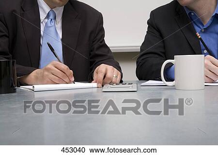 Two businessmen working at a table View Large Photo Image Stock Image - Two businessmen working at a table. Fotosearch