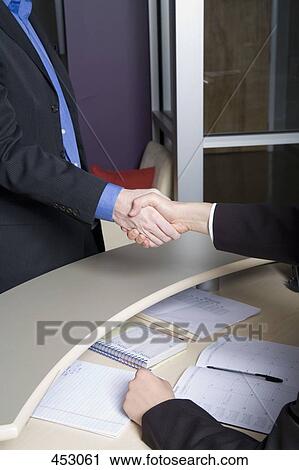 Two men shaking hands over a desk View Large Photo Image Stock Image - Two men shaking hands over a desk. Fotosearch