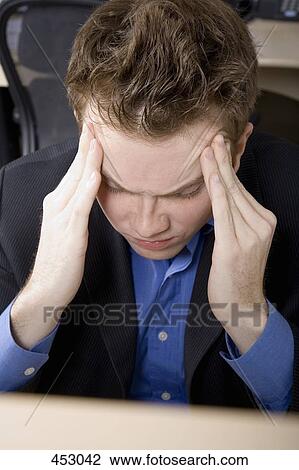 Young businessman rubbing forehead whilst sitting at a desk View Large Photo Image Stock Image - Young businessman rubbing forehead whilst sitting at a desk. Fotosearch