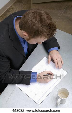 Young businessman sitting at a desk and writing in a personal organizer View Large Photo Image Stock Image - Young businessman sitting at a desk and writing in a personal organizer. Fotosearch