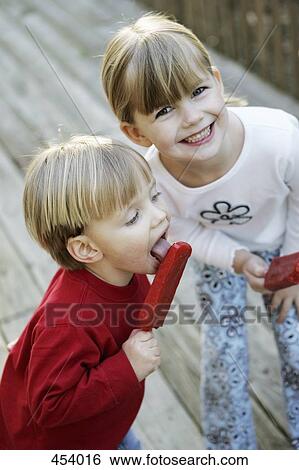 Stock Photograph - A boy and a girl eating popsicles in a back yard. Fotosearch