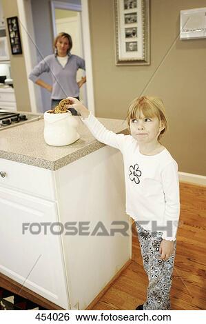 Stock Photograph - A mother watching her daughter take a cookie from a jar on the kitchen counter. Fotosearch