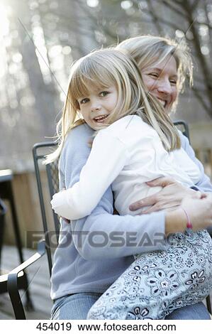 Mother and daughter embracing whilst sitting on the patio View Large Photo Image Stock Photo - Mother and daughter embracing whilst sitting on the patio. Fotosearch