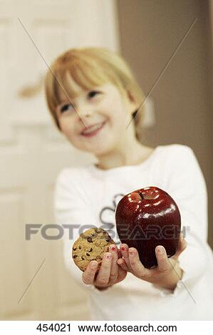 Young girl holding a chocolate chip cookie in one hand and an apple in the other View Large Photo Image Stock Image - Young girl holding a chocolate chip cookie in one hand and an apple in the other. Fotosearch